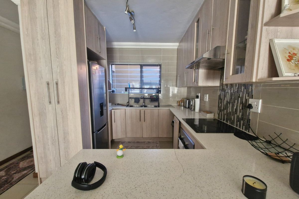 A functional kitchen featuring light wood-grain cabinetry, stone countertops, a built-in electric hob with extractor, and a tiled backsplash.