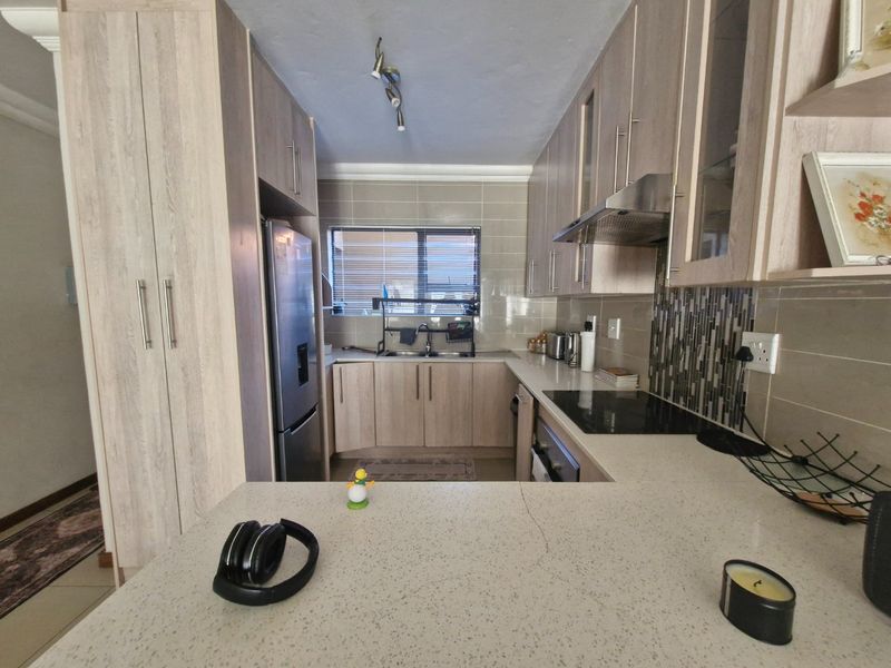A functional kitchen featuring light wood-grain cabinetry, stone countertops, a built-in electric hob with extractor, and a tiled backsplash.