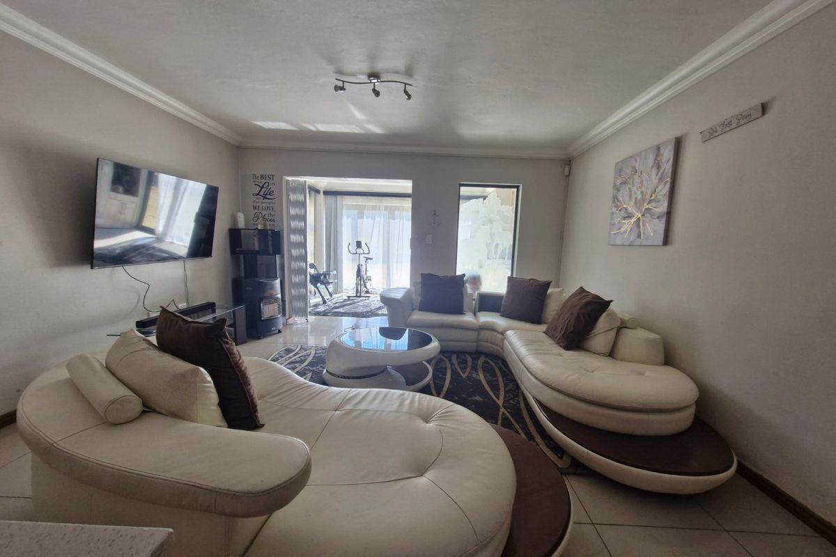 Spacious living room featuring tiled flooring, ceiling coving, and large sliding glass doors providing access to an adjacent patio area.