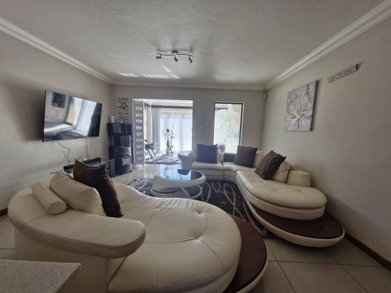 Spacious living room featuring tiled flooring, ceiling coving, and large sliding glass doors providing access to an adjacent patio area.