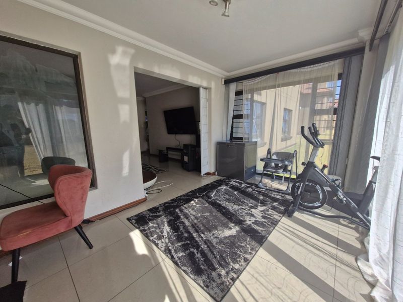 A bright living area featuring large windows, tiled flooring, and a coved ceiling, providing a versatile space with direct access to adjacent rooms.