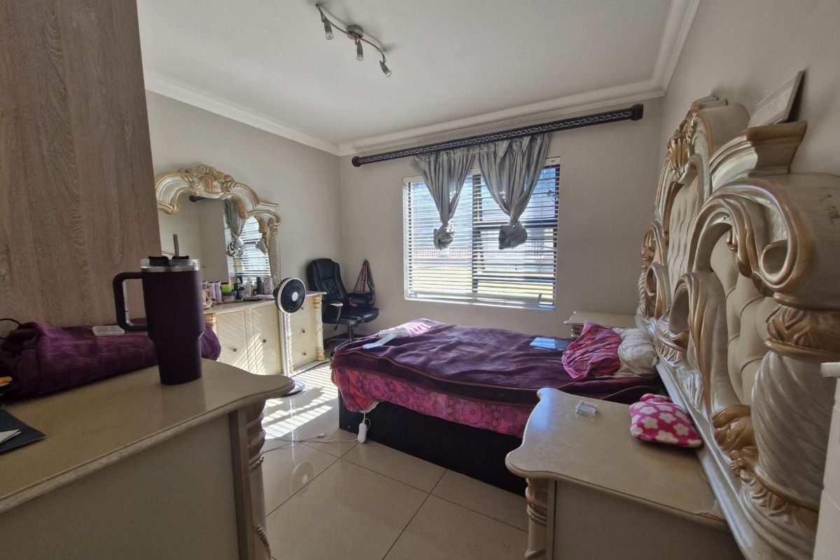 A spacious bedroom featuring tiled flooring, coved cornicing, and a large window fitted with venetian blinds and decorative curtain rods.
