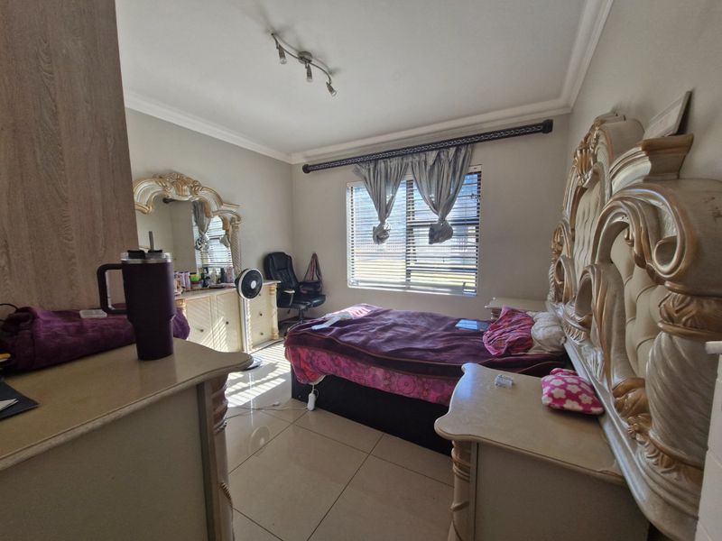A spacious bedroom featuring tiled flooring, coved cornicing, and a large window fitted with venetian blinds and decorative curtain rods.