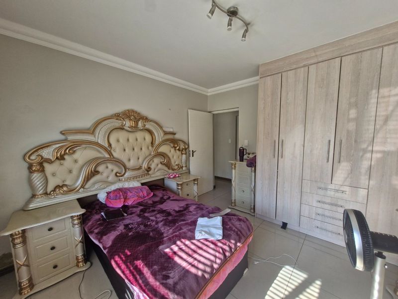 A well-maintained bedroom featuring built-in wooden cupboards, tiled flooring, and modern track lighting, offering a functional and comfortable living space.