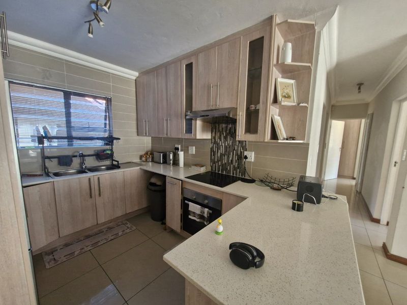 Modern kitchen featuring light wood-finish cabinetry, stone countertops, integrated electric hob and oven, and a tiled backsplash with a functional breakfast bar.