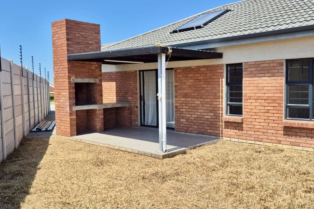 Rear exterior view featuring a covered patio with a built-in brick braai, enclosed by a precast boundary wall with electric fencing.