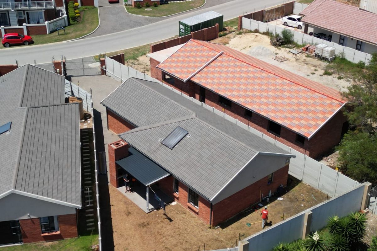 Aerial view of a residential property featuring a brick house with a tiled roof, solar water heater, and a covered patio area.