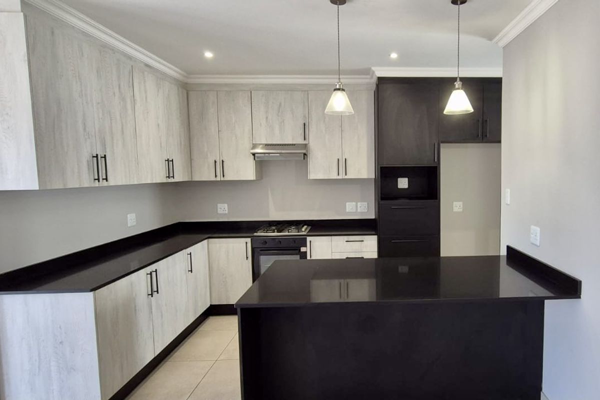 Modern kitchen featuring two-tone cabinetry, dark stone countertops, integrated gas hob, oven, extractor fan, and a functional breakfast bar island.