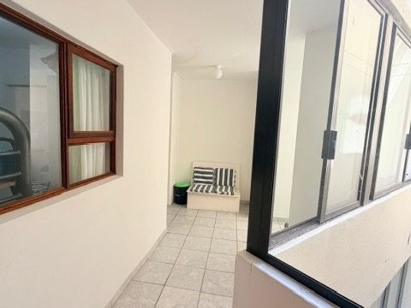 A covered balcony or walkway area featuring tiled flooring and large sliding glass windows, providing a bright and functional outdoor transition space.