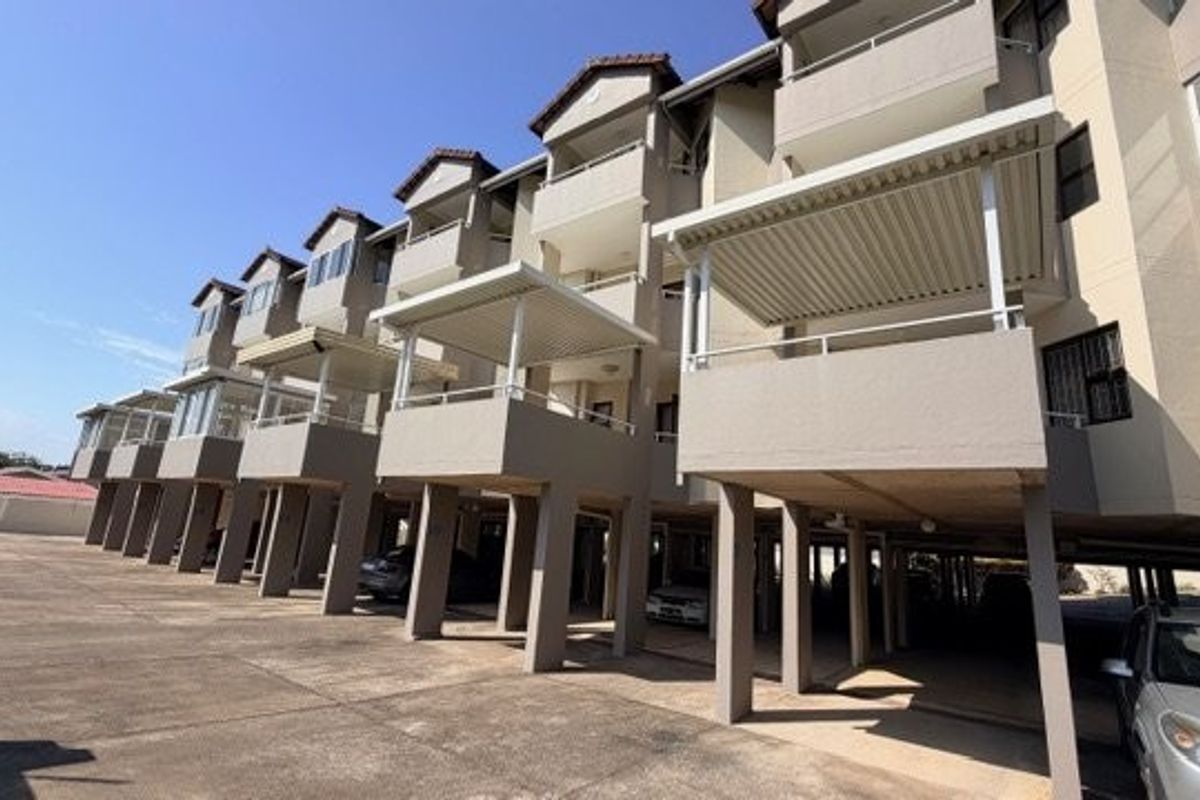 Exterior view of an apartment complex featuring elevated balconies with covered patios and ground-level undercover parking bays.