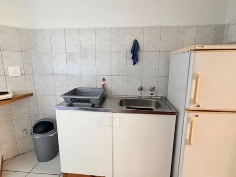 Compact kitchen area featuring a stainless steel sink, tiled splashback, and basic cabinetry, providing a functional space for meal preparation.