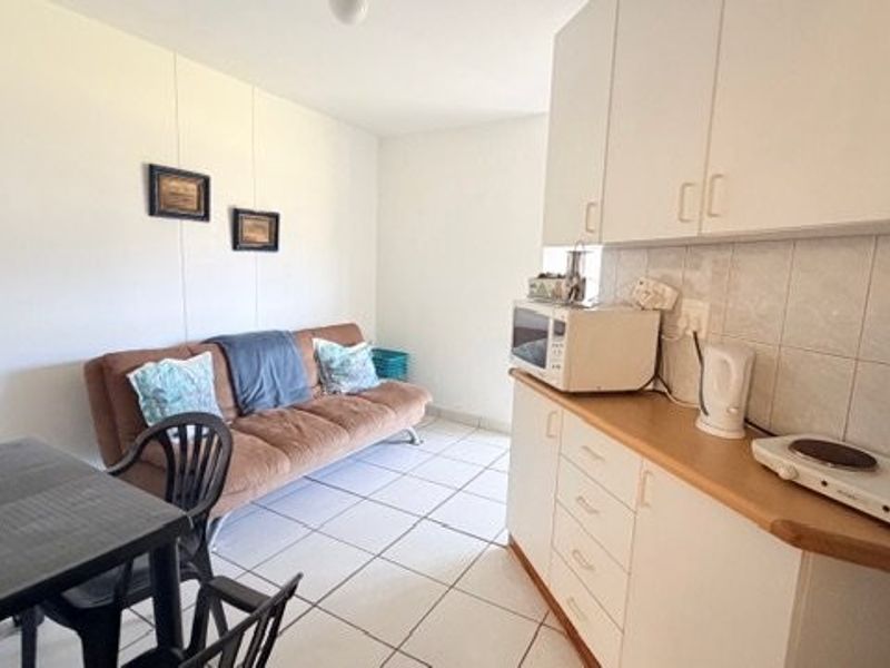 Open-plan living area featuring a compact kitchenette with built-in cabinetry, tiled backsplash, and tiled flooring throughout.