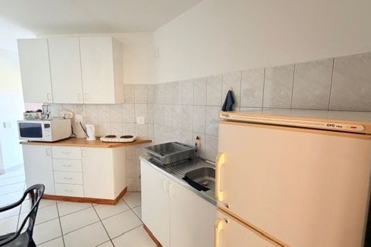 A compact kitchen featuring white built-in cabinetry, tiled backsplash, and tiled flooring, offering a functional layout with basic preparation space.