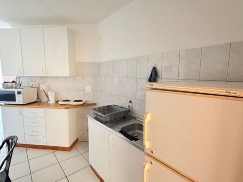 A compact kitchen featuring white built-in cabinetry, tiled backsplash, and tiled flooring, offering a functional layout with basic preparation space.