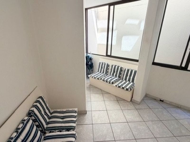 A covered balcony area featuring tiled flooring and large sliding glass windows, providing a bright and functional outdoor living space.