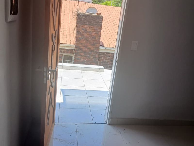 An open doorway leading to a tiled balcony area with views of neighboring rooftops.
