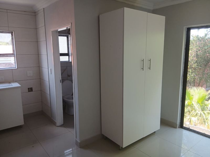 A bright, empty bedroom featuring tiled flooring, a built-in cupboard, and direct access to an en-suite bathroom with large windows.