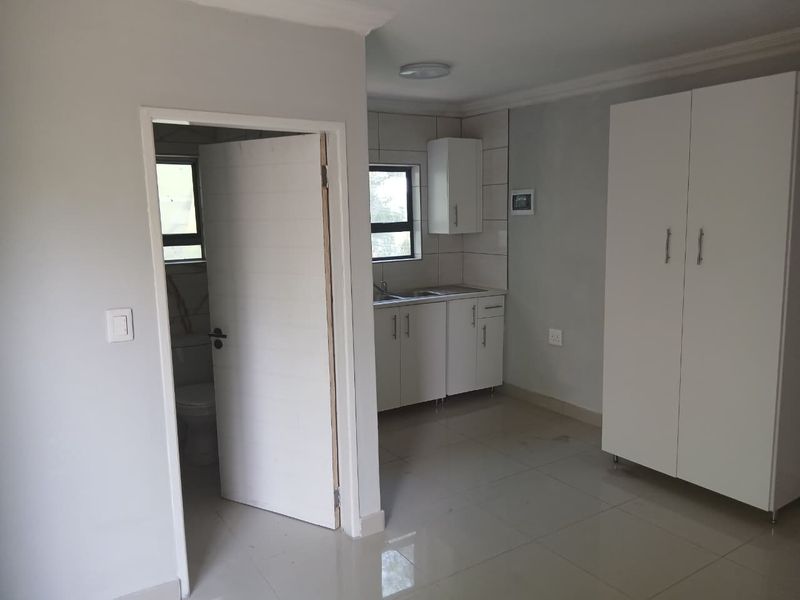 Open plan living area featuring tiled floors, built-in kitchen cabinetry with sink, and a built-in wardrobe, adjacent to a separate bathroom entrance.