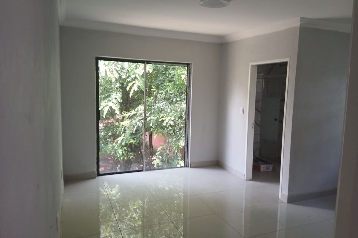 A bright, empty bedroom featuring neutral tiled flooring, a sliding glass door with garden views, and clean white walls.
