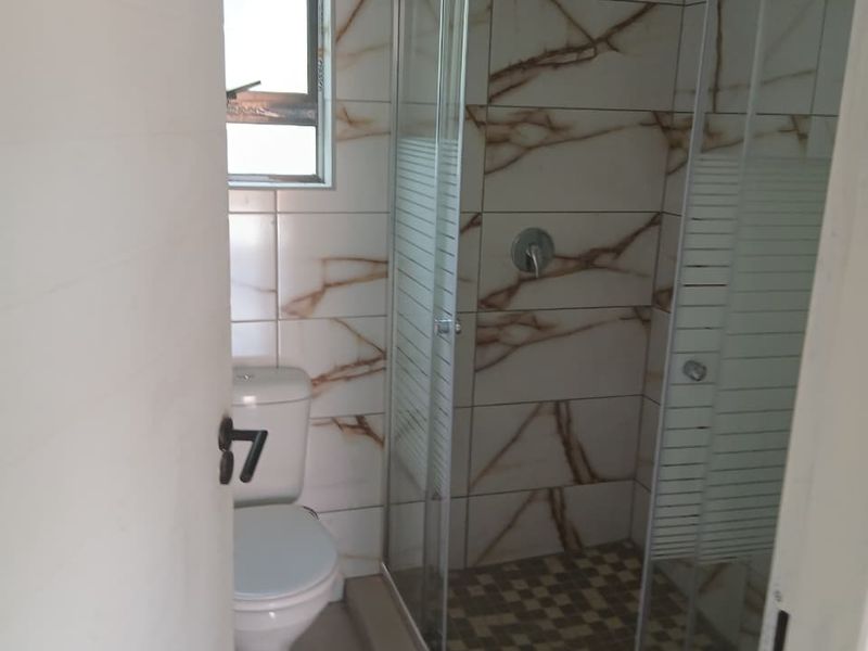 A compact bathroom featuring a glass-enclosed shower with a rain shower head, a standard toilet, and modern marble-effect wall tiling.
