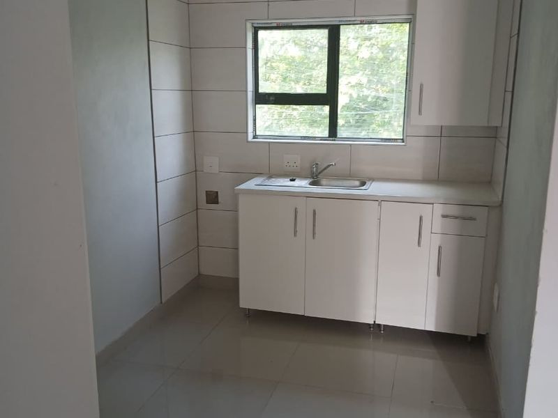 A compact, empty kitchen featuring white cabinetry, a stainless steel sink, tiled splashbacks, and polished floor tiles, ready for appliance installation.