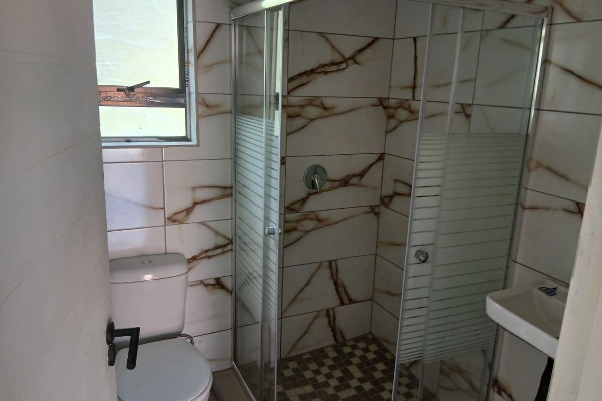 Compact bathroom featuring a glass shower enclosure, toilet, and wall-mounted basin with marble-effect wall tiling and mosaic floor tiles.