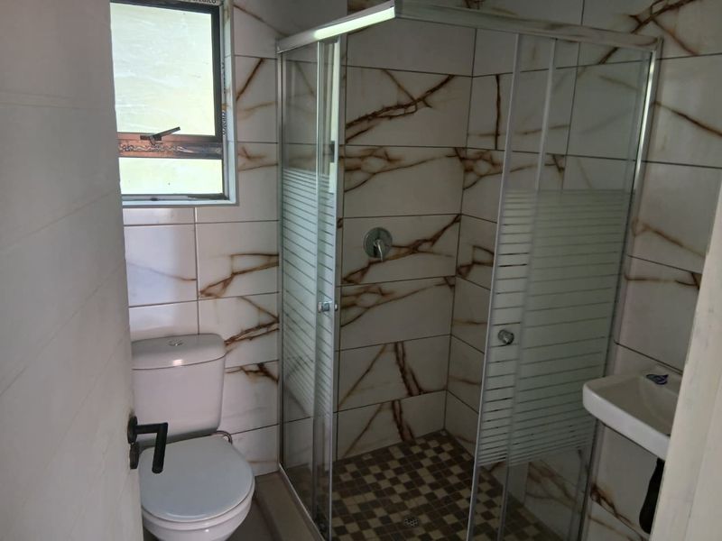 Compact bathroom featuring a glass shower enclosure, toilet, and wall-mounted basin with marble-effect wall tiling and mosaic floor tiles.