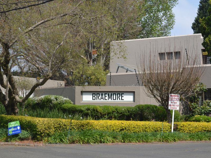 Street view of the Braemore townhouse complex entrance, featuring perimeter walling, electric fencing, and established landscaped garden beds.