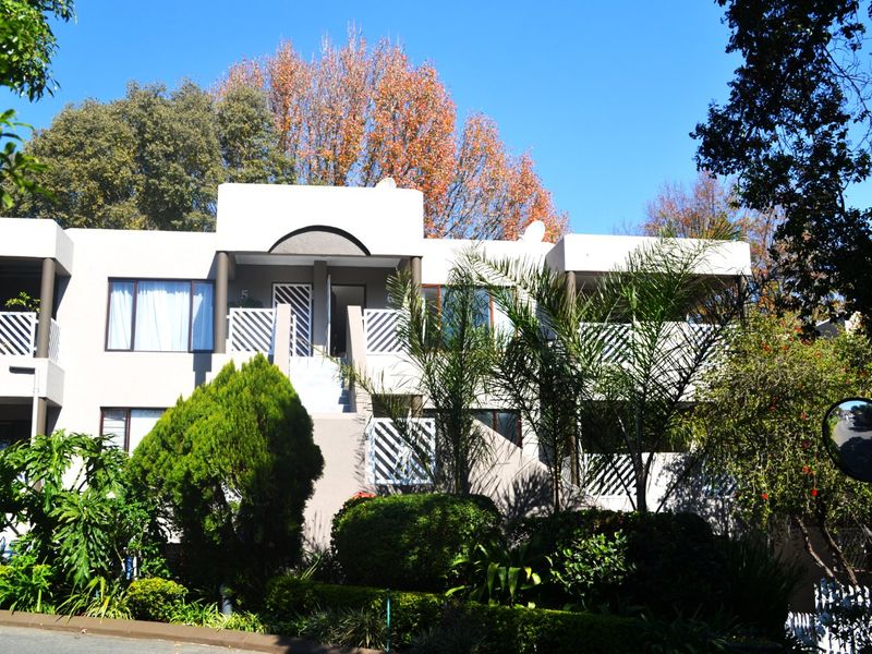Front elevation of a multi-level townhouse complex featuring balconies, concrete balustrades, and established garden landscaping.