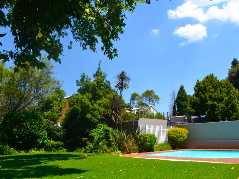 A well-maintained private garden featuring a swimming pool with brick coping, surrounded by established trees and perimeter boundary walls.