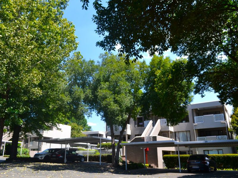 Exterior view of the townhouse complex featuring covered parking bays, mature trees, and multi-level residential units with balconies.