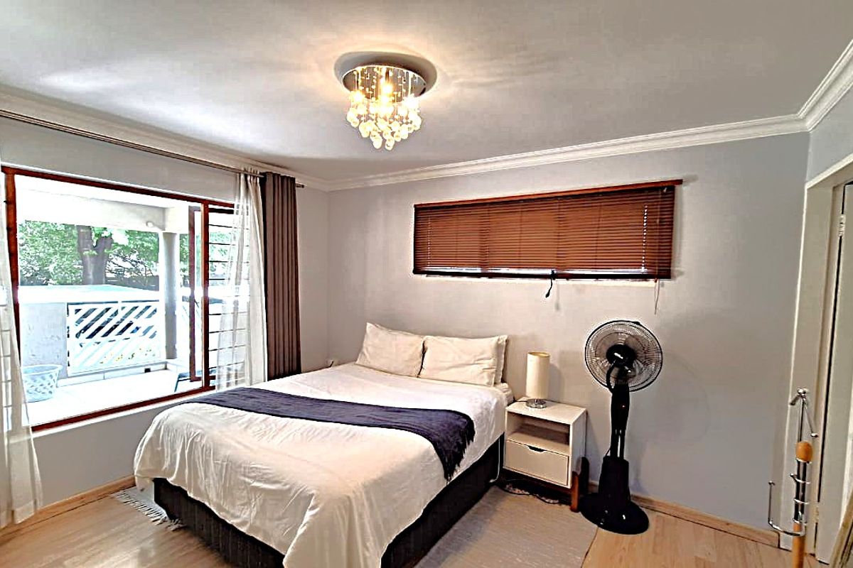 A well-lit bedroom featuring laminate flooring, crown molding, and a large sliding door providing direct access to an outdoor patio area.