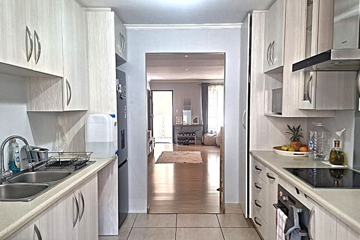 A functional galley-style kitchen featuring light wood-grain cabinetry, stone-look countertops, a built-in oven, and a glass cooktop with an extractor fan.