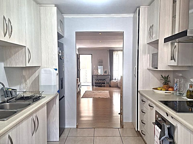 A functional galley-style kitchen featuring light wood-grain cabinetry, stone-look countertops, a built-in oven, and a glass cooktop with an extractor fan.