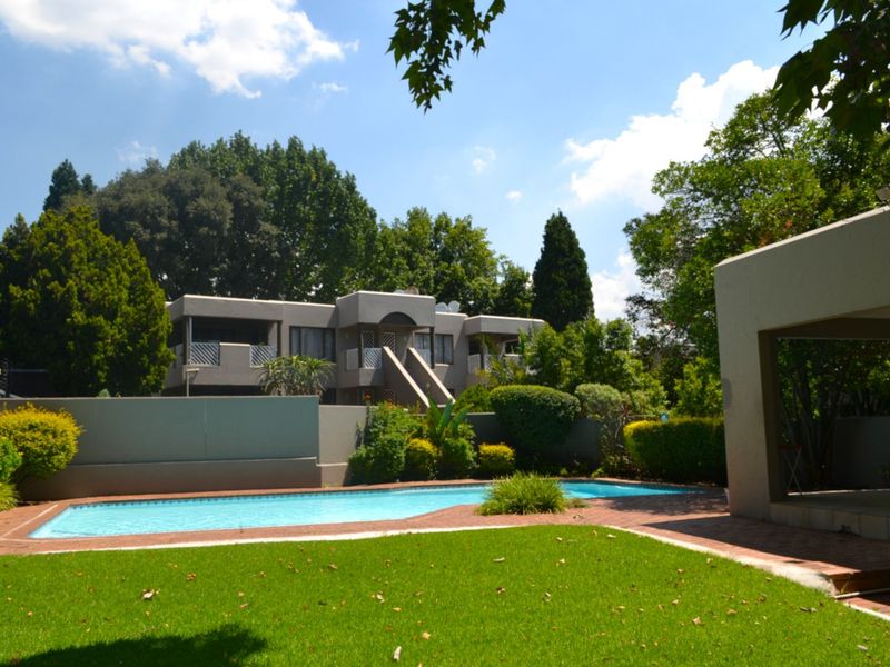A well-maintained communal swimming pool area featuring a paved surround, manicured lawn, and views of the townhouse complex architecture.