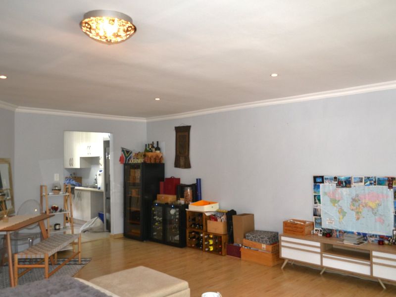 Open plan living area featuring laminate flooring, recessed ceiling lighting, and a decorative flush-mount light fixture, with an adjacent kitchen visible.