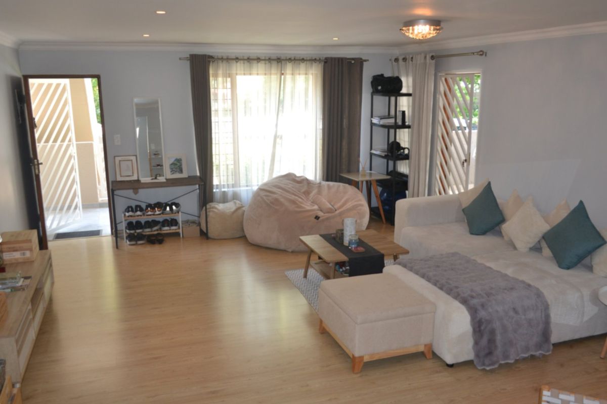 Spacious living room featuring light wood-look laminate flooring, recessed downlighting, and direct access to an outdoor patio area through a security gate.