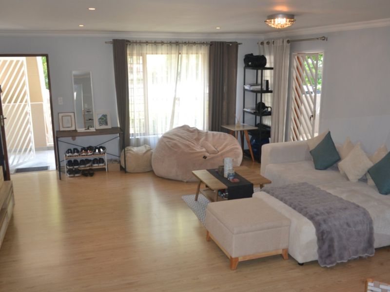 Spacious living room featuring light wood-look laminate flooring, recessed downlighting, and direct access to an outdoor patio area through a security gate.