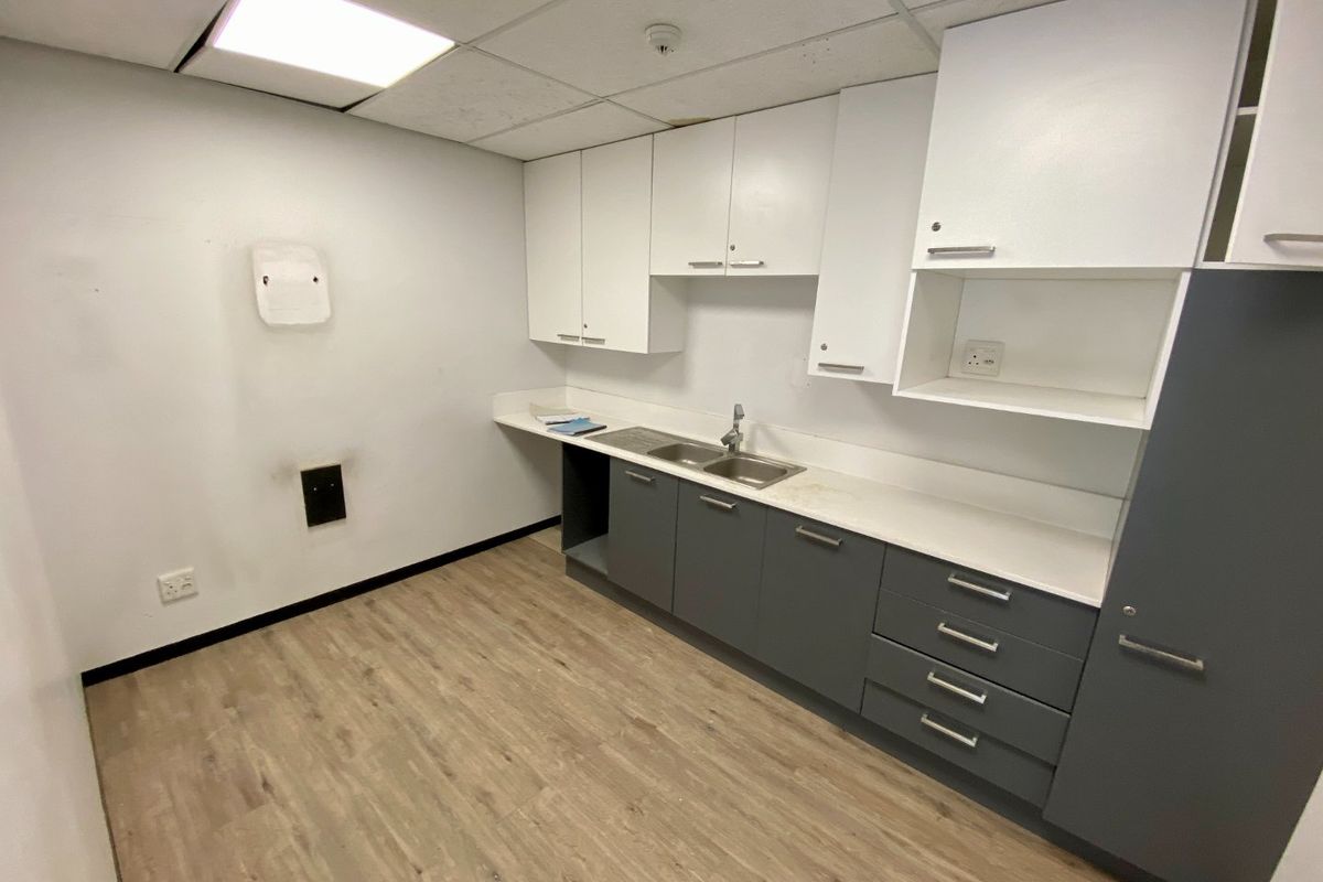 A functional kitchenette featuring modern grey and white cabinetry, a stainless steel double sink, and durable laminate flooring in a clean, empty space.