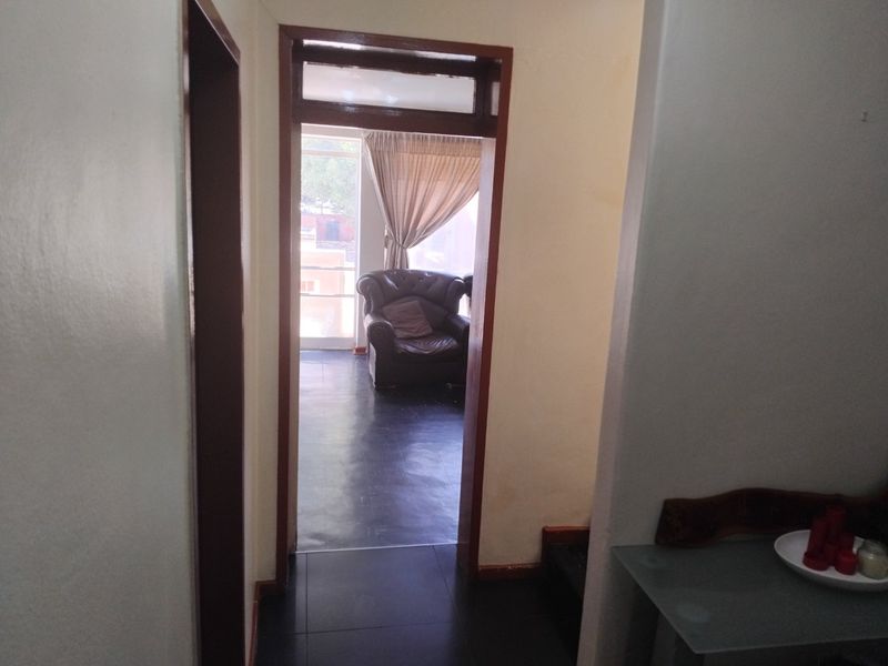 A view through a hallway with dark tiled flooring and wooden door frames, leading into an adjacent living space.