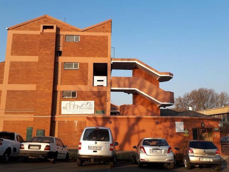 Exterior view of a multi-story brick apartment building featuring an external concrete staircase and ground-level parking area.