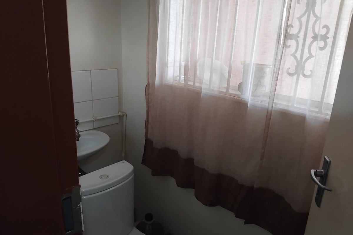 A compact bathroom featuring a standard toilet, wall-mounted washbasin, and a window fitted with security bars.