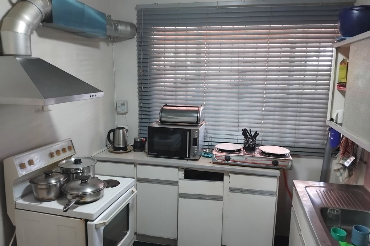 A compact kitchen featuring a freestanding stove, stainless steel sink, and built-in cabinetry with some visible wear and missing hardware.