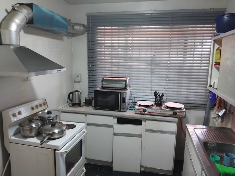 A compact kitchen featuring a freestanding stove, stainless steel sink, and built-in cabinetry with some visible wear and missing hardware.