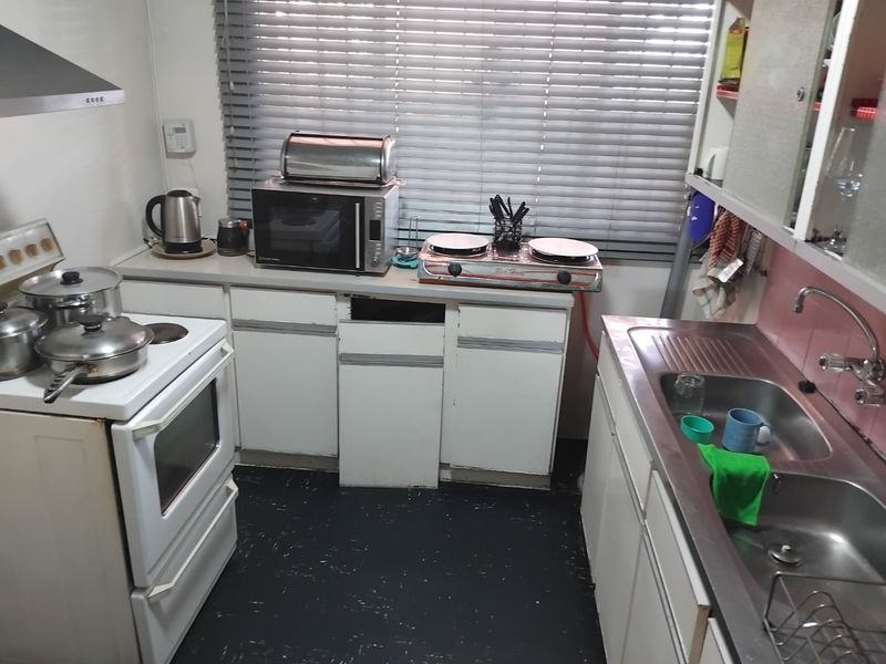 A compact kitchen featuring a stainless steel sink, freestanding stove, extractor fan, and built-in cabinetry with a missing cabinet door.