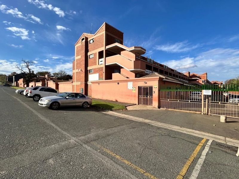 Exterior view of an apartment complex featuring a brick facade, perimeter wall, and gated entrance from the street.