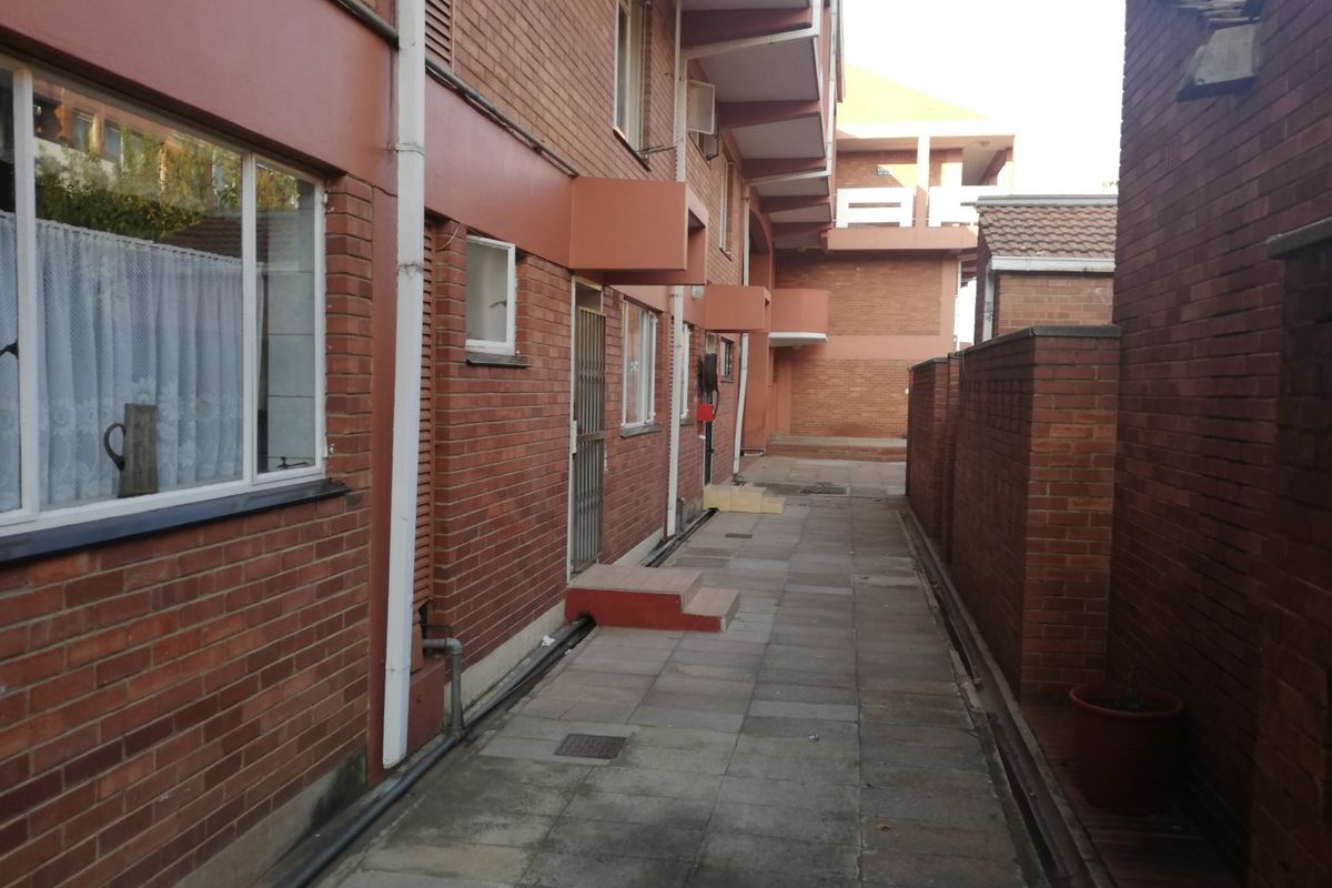 A view of the rear exterior walkway of the apartment complex, featuring brick facade construction and paved access paths.