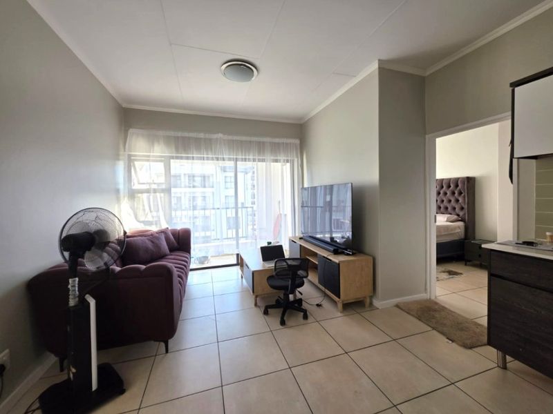 A bright living room featuring tiled flooring and a sliding glass door leading to a balcony, with an adjacent view into the bedroom.
