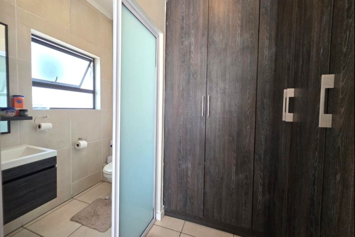 Modern bathroom featuring dark wood-grain built-in cabinetry, a sleek vanity, tiled finishes, and a frosted glass sliding door for privacy.
