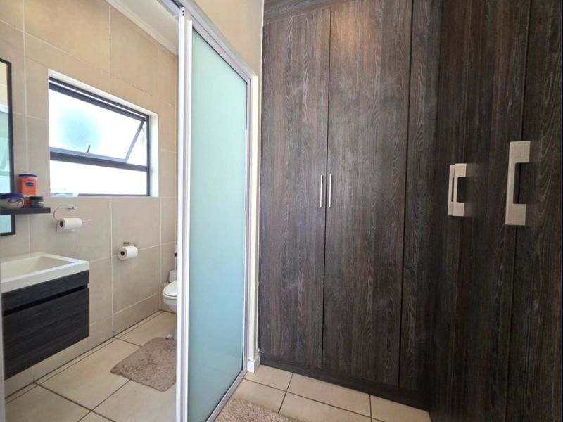 Modern bathroom featuring dark wood-grain built-in cabinetry, a sleek vanity, tiled finishes, and a frosted glass sliding door for privacy.
